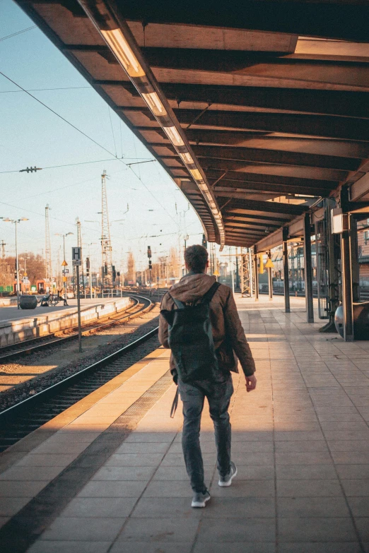 a man with a backpack walking towards a train station, by Niko Henrichon, pexels contest winner, happening, sunny morning, 🚿🗝📝