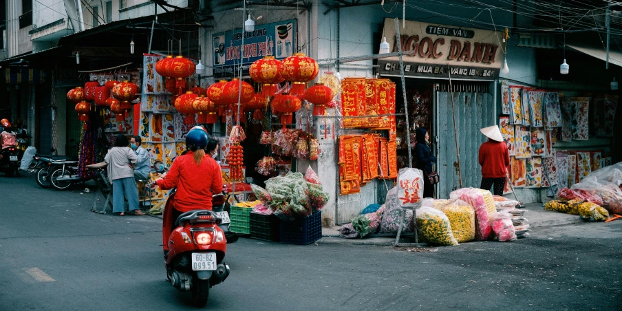 a person riding a motor scooter down a street, by Julia Pishtar, pexels contest winner, chinese lanterns, market setting, red adornments, flowers around