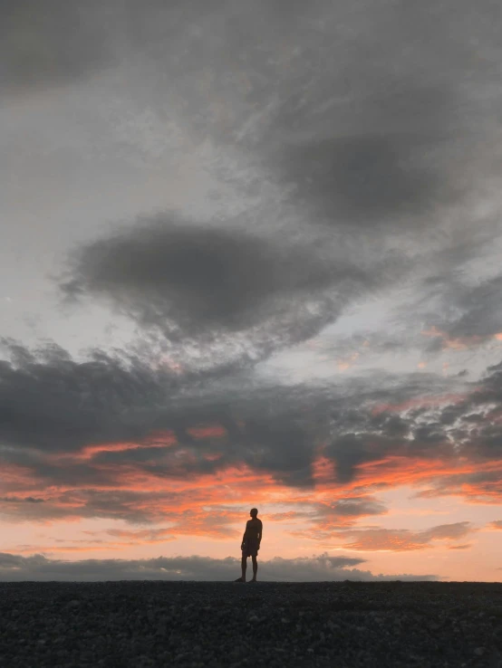 a person standing on top of a beach under a cloudy sky, during a sunset, profile picture