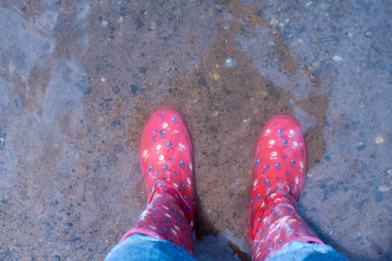 a person wearing red rain boots standing in a puddle, pexels, paisley, flat colour, sea underneath, alana fletcher