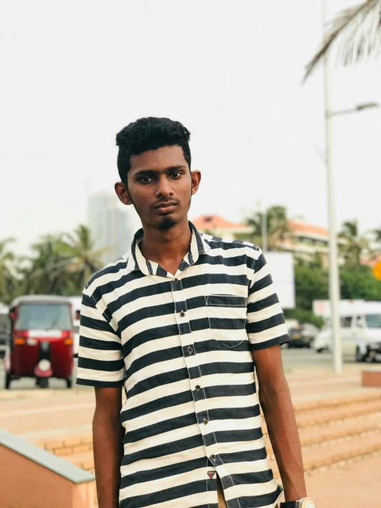 a man in a striped shirt holding a skateboard, by Max Dauthendey, hurufiyya, colombo sri lanka cityscape, he is about 20 years old | short, profile image