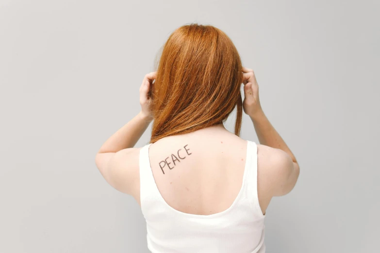 a woman with the word peace written on her back, a tattoo, trending on pexels, long ginger hair, plain background, shot on sony a 7, white porcelain skin