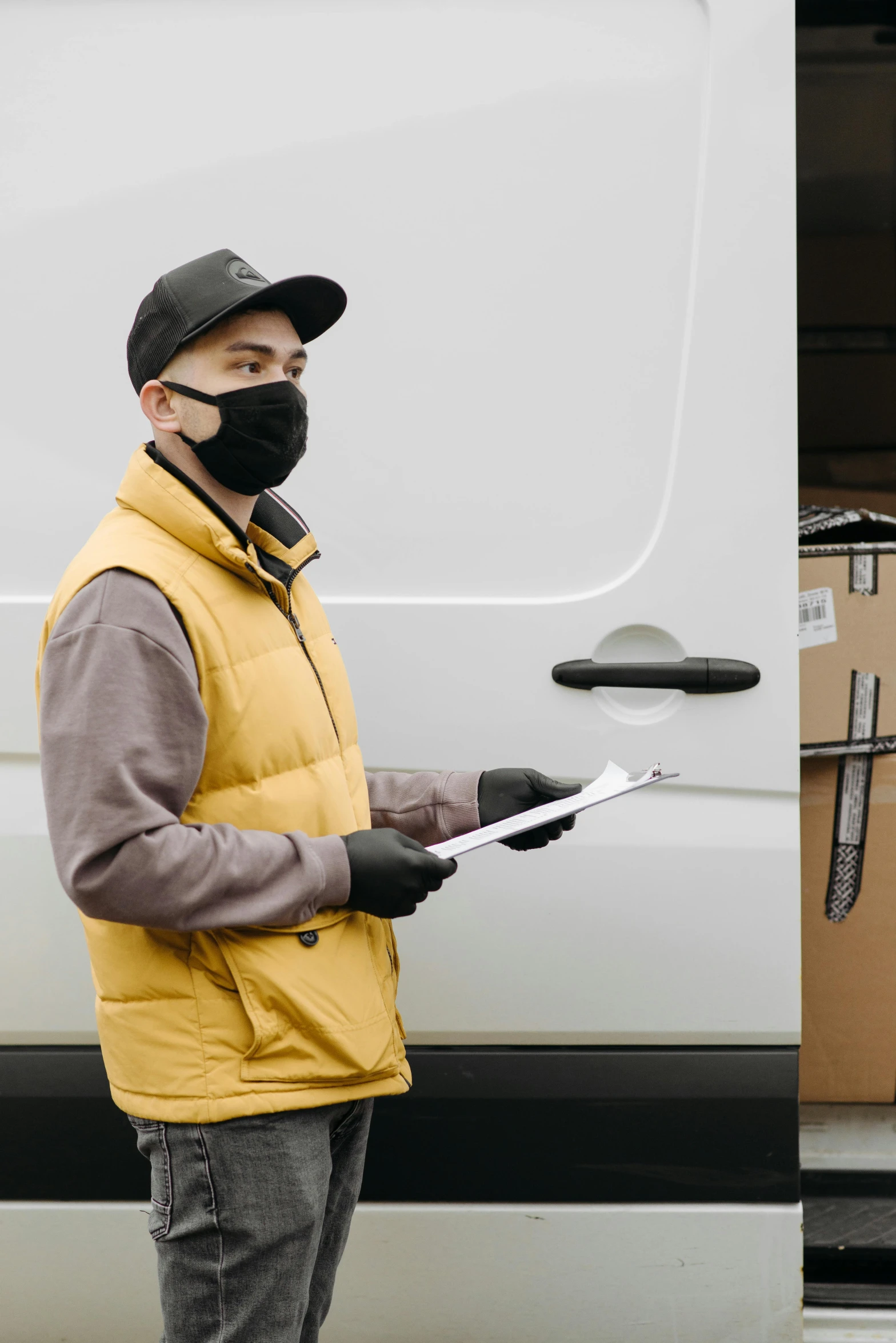 a man in a yellow vest standing next to a white van, shutterstock, balaclava mask, cardboard, document photo, brown