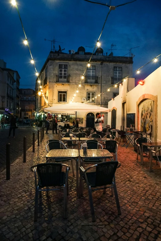 a couple of tables sitting on top of a cobblestone street, lisbon city at night, market setting, bar, outside