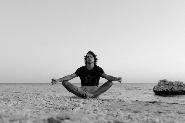 a black and white photo of a man meditating on the beach, red sea, robert sheehan, simone graci, symmetrical pose