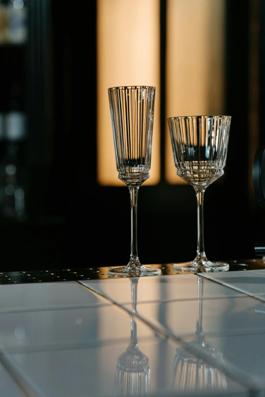 a couple of wine glasses sitting on top of a counter, inspired by Ramon Pichot, baroque, refracted lines and sparkles, onyx, evening light, champagne