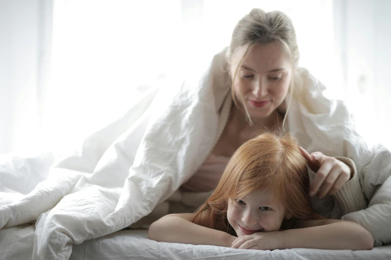 a woman laying on top of a bed next to a little girl, pexels contest winner, redhead woman, 15081959 21121991 01012000 4k, covered with blanket, white hue