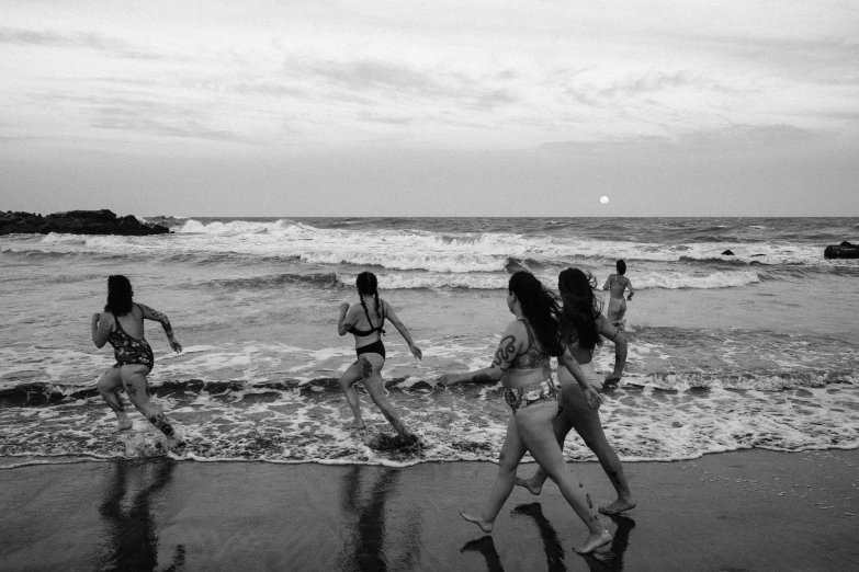 a group of women walking along a beach next to the ocean, a black and white photo, inspired by Larry Fink, unsplash contest winner, renaissance, playing soccer at the beach, set on night, swimming in ocean, anna nikonova