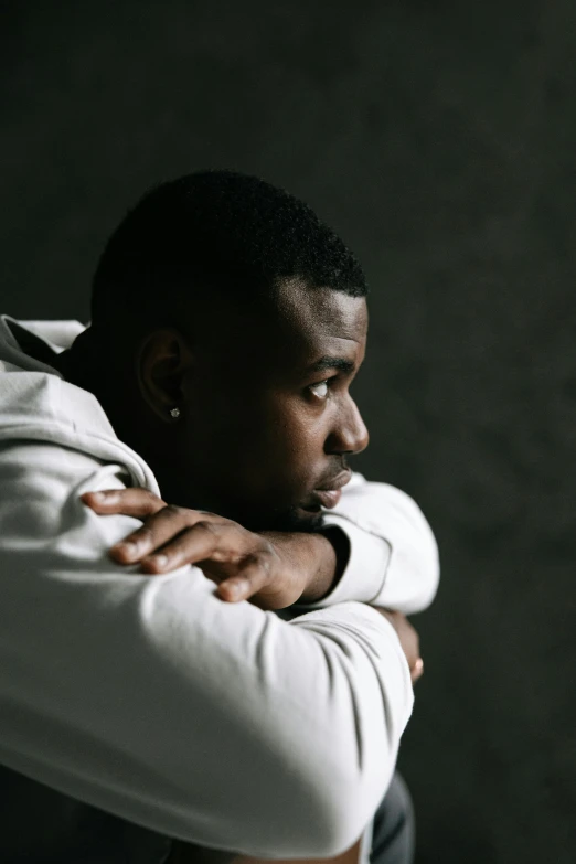 a man leaning against a wall with his arms crossed, inspired by Paul Georges, trending on pexels, depressed sad expression, jaylen brown, looking from shoulder, man wearing a closed cowl