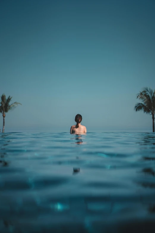 a man sitting in the middle of a swimming pool, by Carey Morris, pexels contest winner, with palm trees in the back, girl looking at the ocean waves, female floating, unsplash 4k