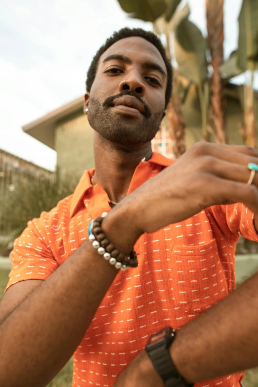 a man in an orange shirt is brushing his teeth, by Fletcher Martin, trending on unsplash, renaissance, bracelets and necklaces, donald glover, poolside, model is wearing techtical vest