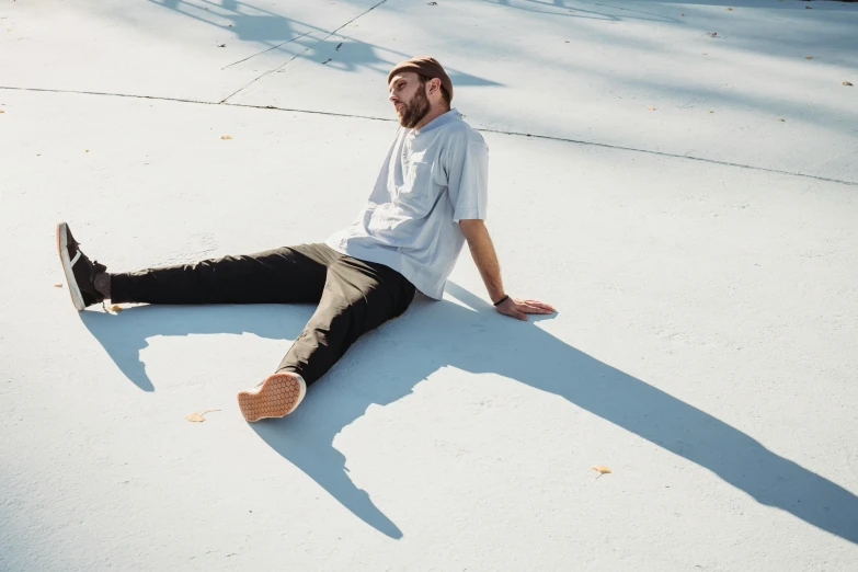 a man sitting on the ground next to a skateboard, an album cover, by Carey Morris, h3h3, long shadow, wearing pants and a t-shirt, uniform off - white sky