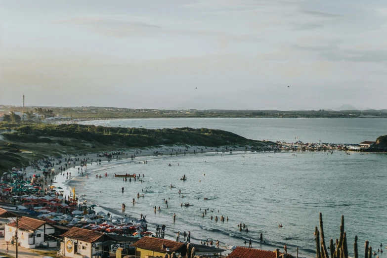 a group of people standing on top of a beach next to a body of water, by Lee Loughridge, pexels contest winner, happening, busy crowds, south african coast, late summer evening, bird's eye view of a city