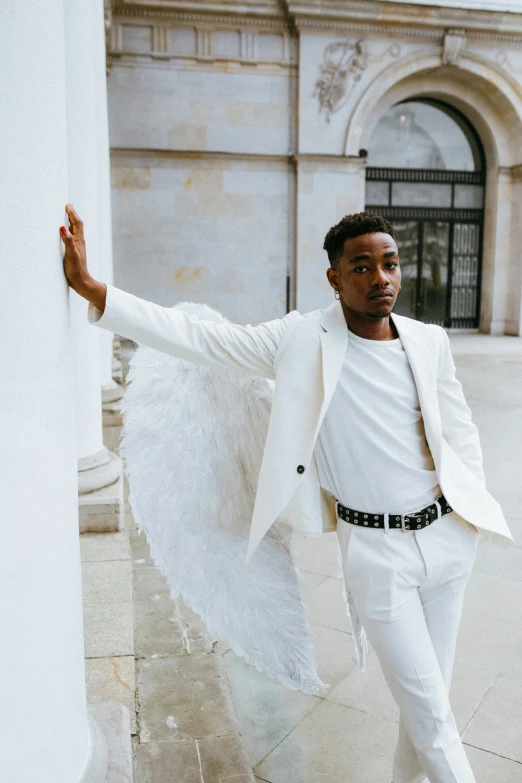 a man in a white suit standing in front of a building, an album cover, inspired by Louis Hersent, pexels contest winner, renaissance, winged boy, mkbhd, non binary model, silver angel wings