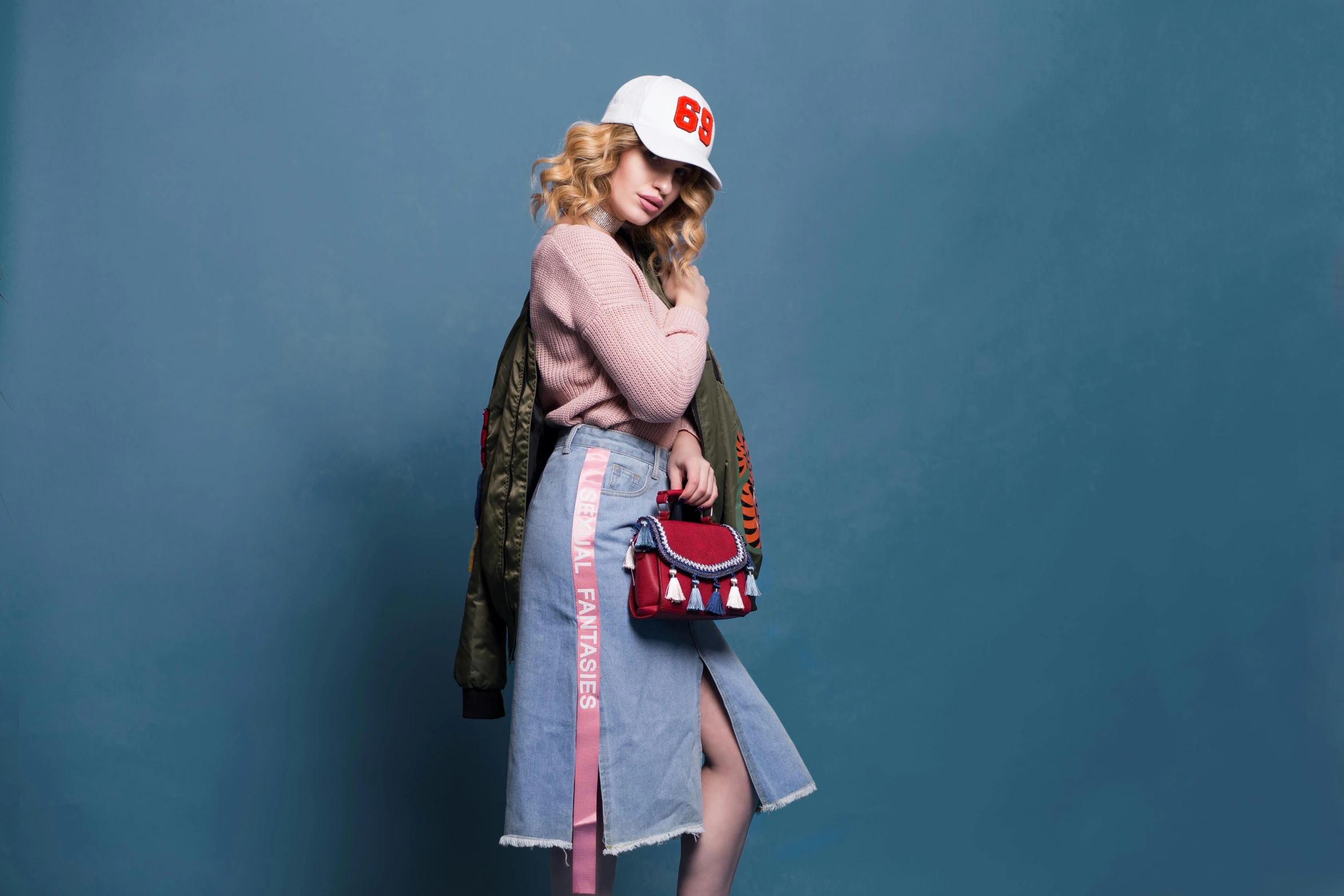 a woman standing in front of a blue wall holding a purse, inspired by Elsa Bleda, trending on pexels, pop art, wearing a baseball cap backwards, taylor swift modeling, pink and red color style, wearing jacket and skirt