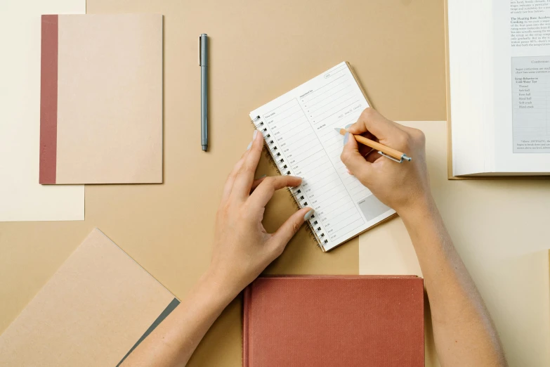 a person writing in a notebook on a desk, trending on pexels, flat lay, brown paper, background image, iconic design