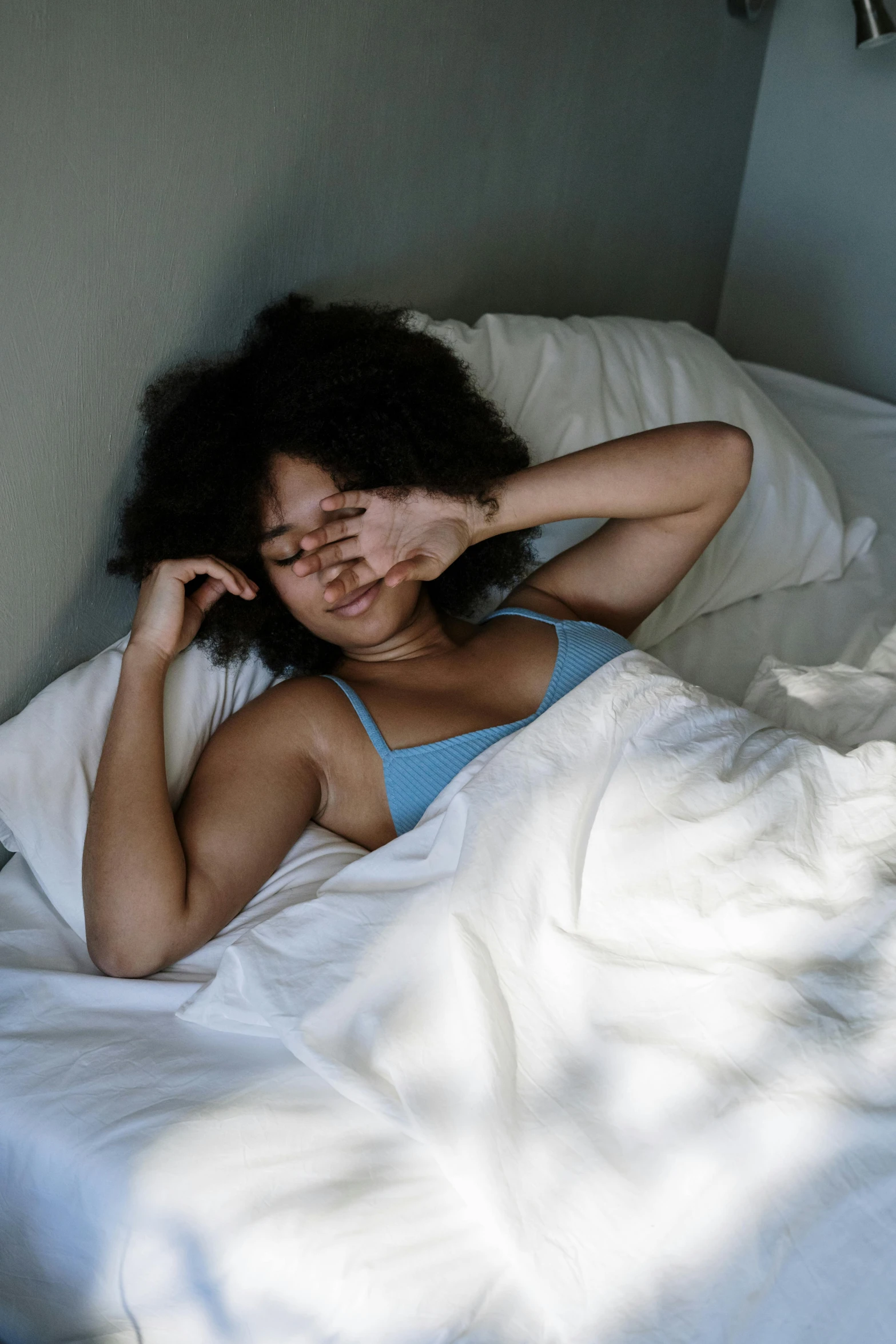 a woman laying in bed with her eyes closed, trending on pexels, renaissance, with afro, blue undergarments, hungover, wearing a light blue shirt