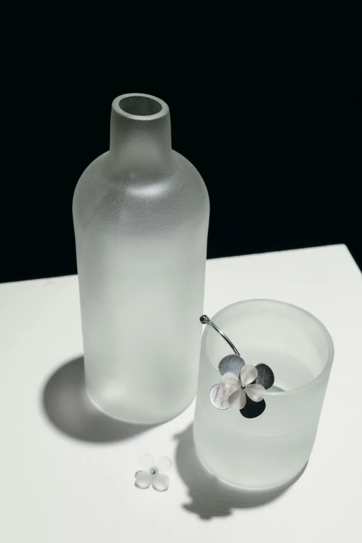 a bottle sitting on top of a table next to a glass, inspired by Robert Mapplethorpe, clover, frosted glass, detail, jewelry