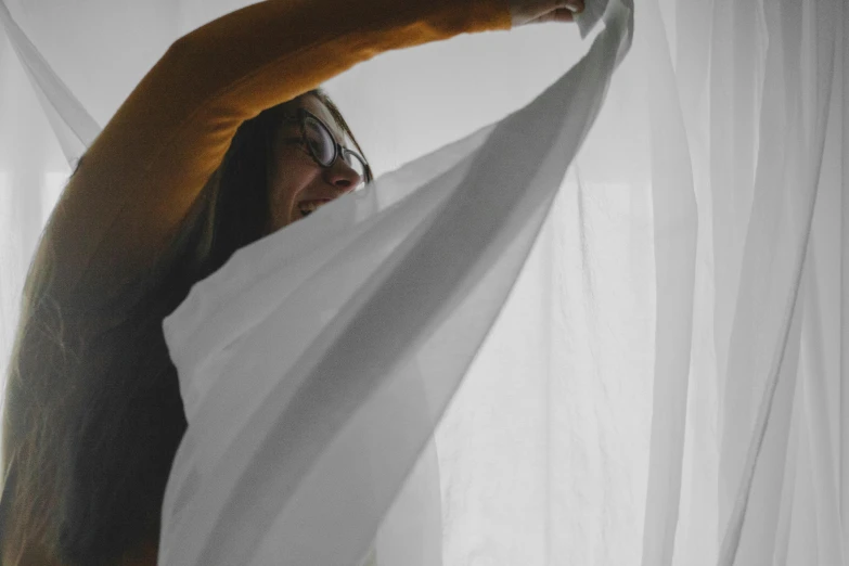 a woman that is standing in front of a curtain, inspired by Christo, pexels contest winner, white sheets, playful composition, waking up, high angle shot