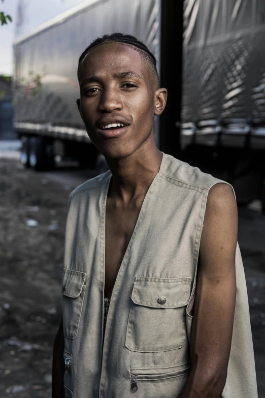 a man standing in front of a truck, by Afewerk Tekle, trending on unsplash, renaissance, androgynous face, wearing a vest, hairless, around 1 9 years old