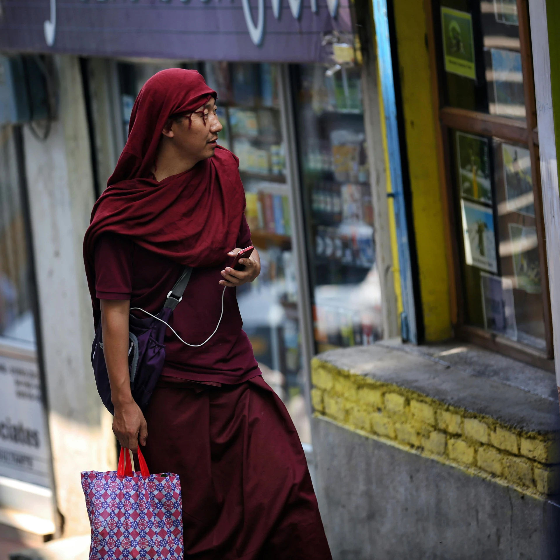 a woman walking down a street with a shopping bag, inspired by Steve McCurry, pexels contest winner, portrait of monk, cellphone, maroon, kalighat