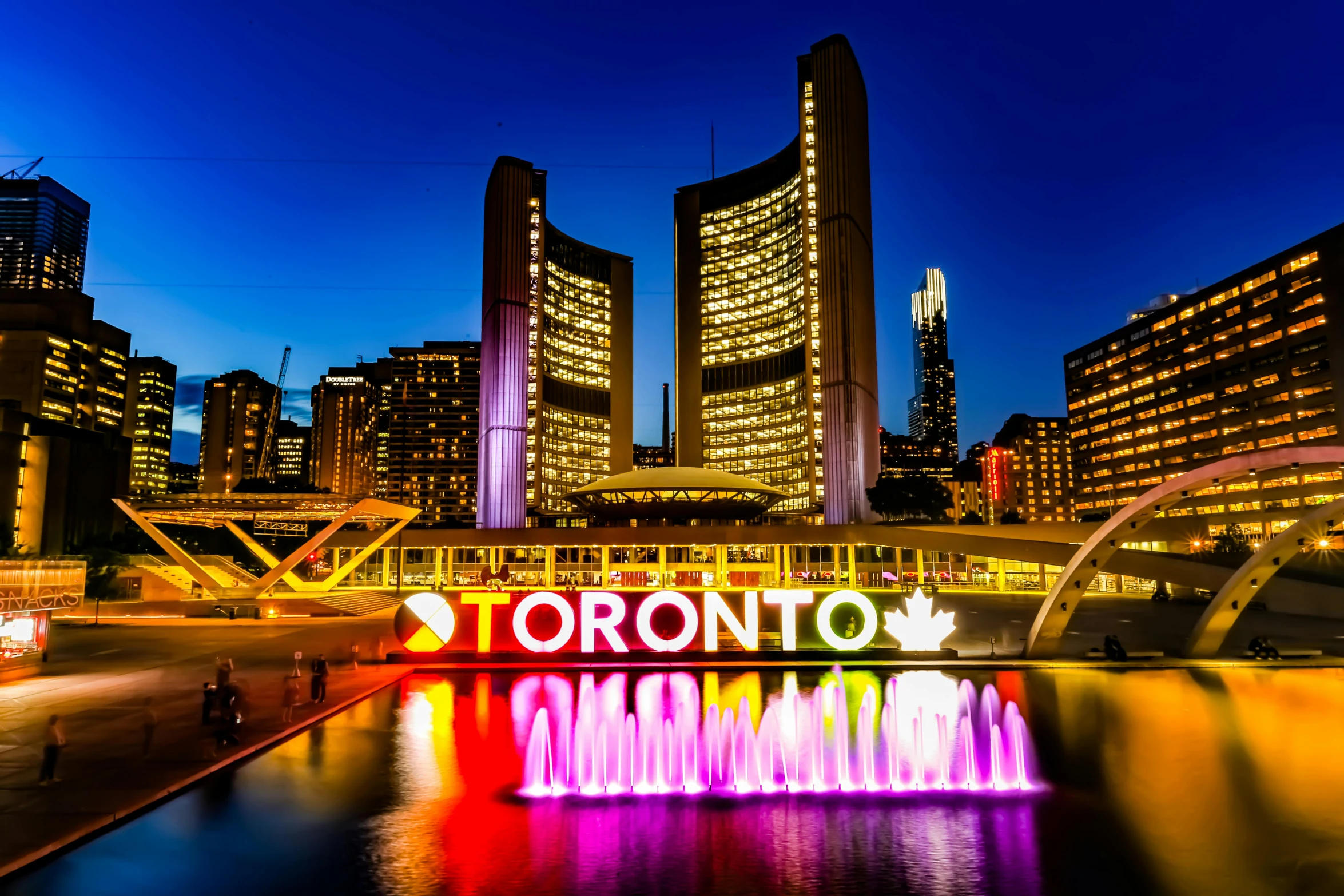 the city skyline is lit up at night, a photo, by Julia Pishtar, the city of toronto, featuring flowing fountains, ad image, travel guide