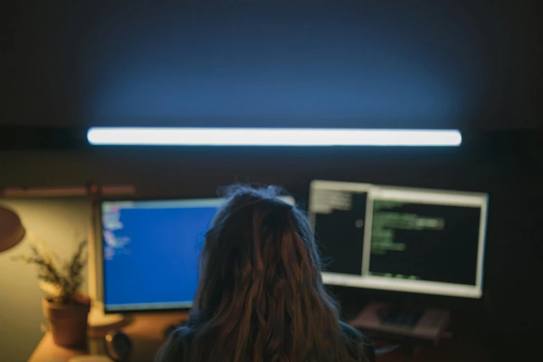 a woman sitting in front of two computer monitors, inspired by Elsa Bleda, pexels, nightime, hacking, a blond, blue light