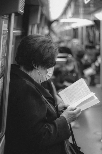 a black and white photo of a woman reading a book, a black and white photo, in a subway, aging, wearing facemask, 15081959 21121991 01012000 4k