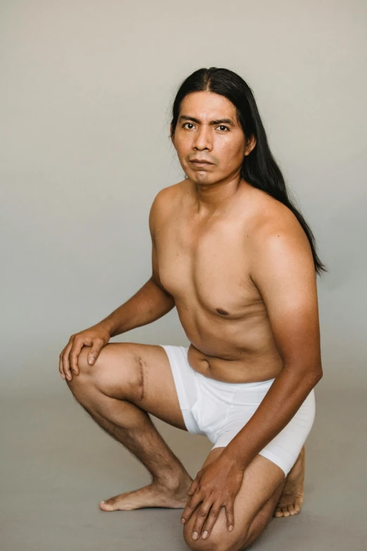 a man sitting on the ground posing for a picture, an album cover, inspired by Jorge Jacinto, white loincloth, studio portrait photo, taken in the early 2020s, full face and body portrait