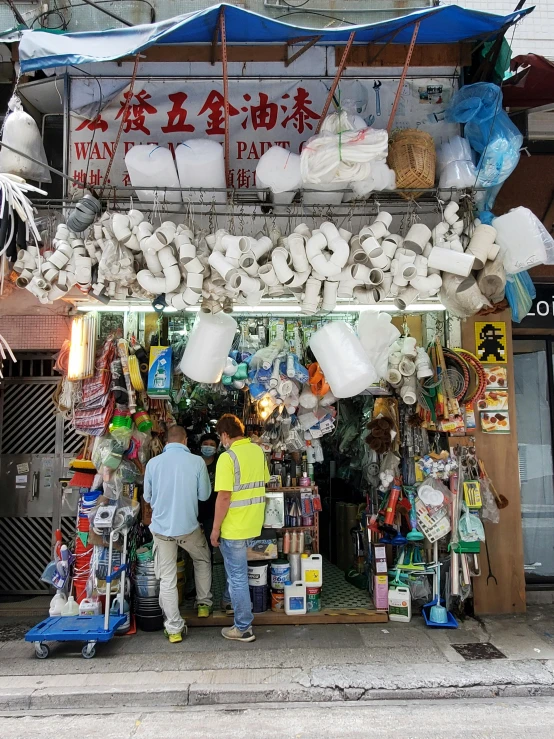 a couple of men standing in front of a store, plasticien, in hong kong, plastic waste, various items, white