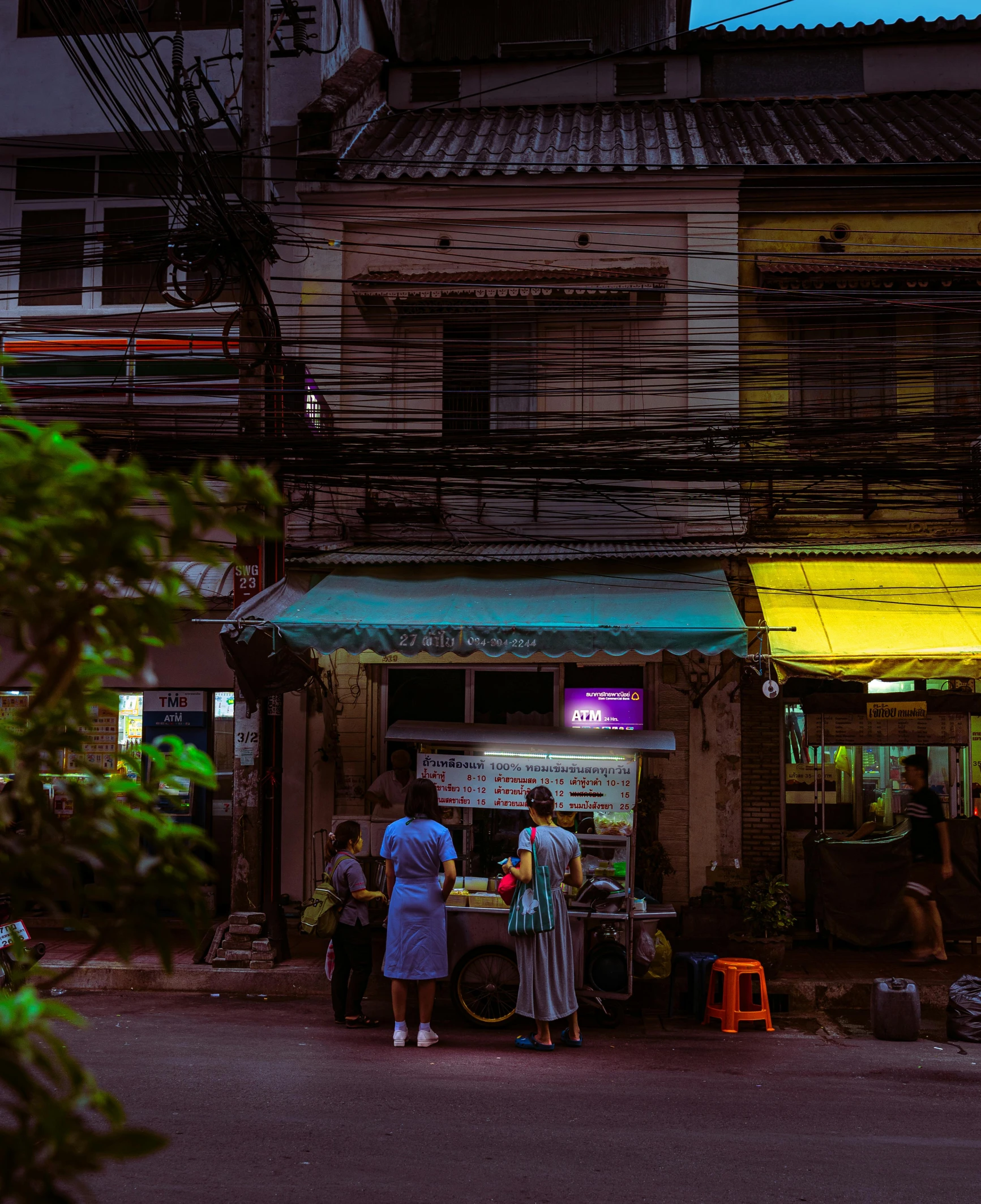 a group of people standing in front of a building, unsplash contest winner, with street food stalls, humid evening, thailand, neighborhood outside window