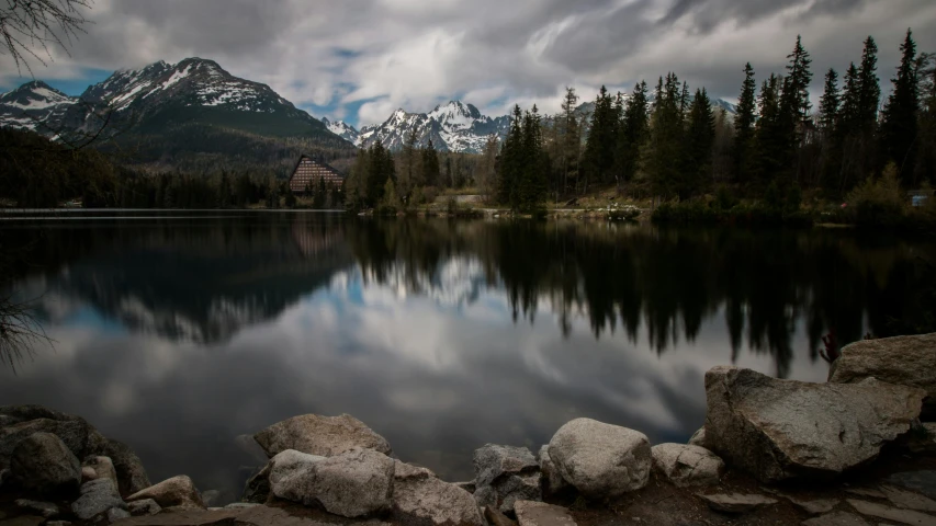 a body of water surrounded by rocks and trees, by Sebastian Spreng, pexels contest winner, dramatic mountains behind, grey, reflects, fine art print