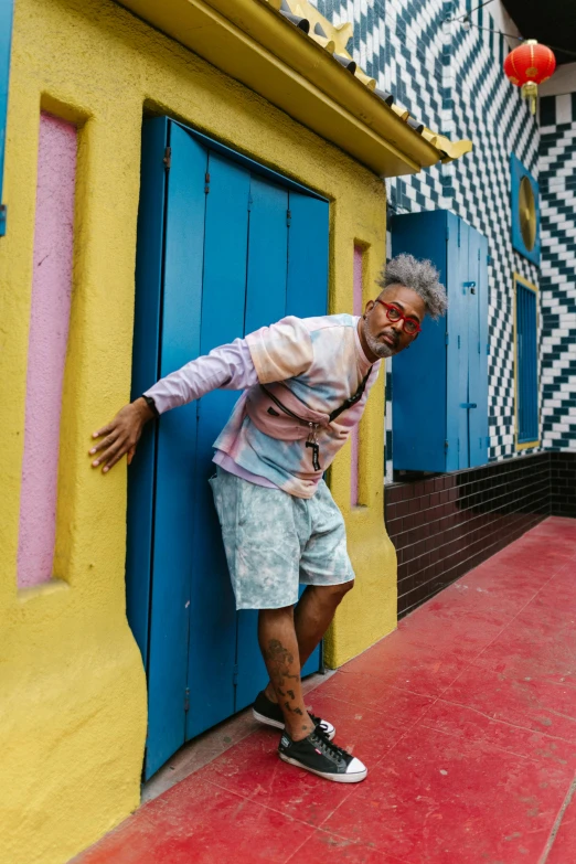 a man leaning against the side of a building, maximalism, colorful striped pavillions, wayne - coyne, exiting from a wardrobe, south beach colors