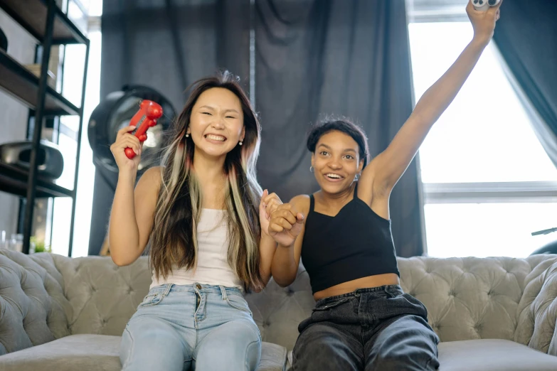 a couple of women sitting on top of a couch, pexels contest winner, holding controller, triumphant pose, varying ethnicities, sport game
