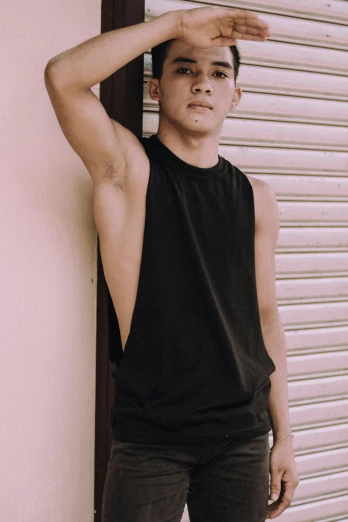 a man standing in front of a garage door, a colorized photo, by Robbie Trevino, trending on pexels, tachisme, wearing a cropped black tank top, set on singaporean aesthetic, non binary model, shaved sides