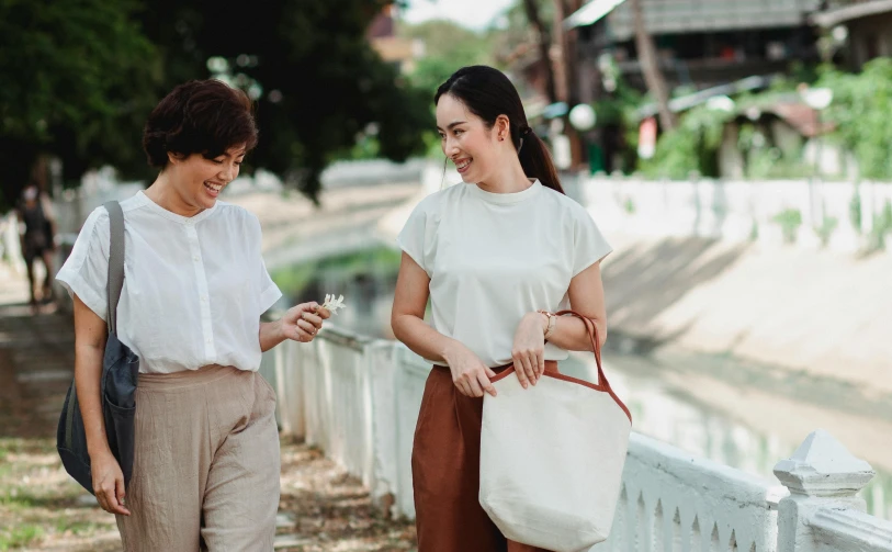 a couple of women standing next to each other on a sidewalk, inspired by Ruth Jên, pexels contest winner, in style of thawan duchanee, bag, wearing a linen shirt, white background