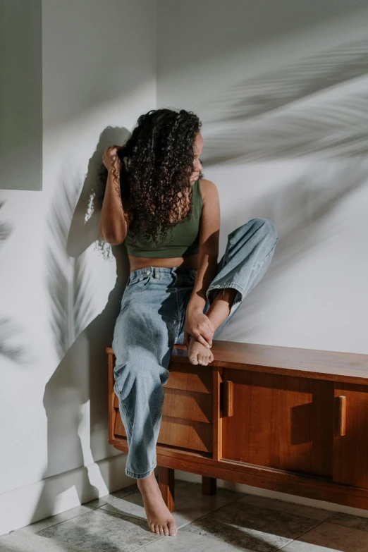 a woman sitting on top of a wooden bench, inspired by Esaias Boursse, trending on pexels, arabesque, standing in corner of room, baggy jeans, curls on top, highly reflective light