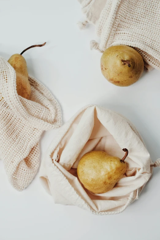 a bag filled with pears sitting on top of a table, a still life, unsplash, cloth wraps, sustainable materials, beige, on a white background