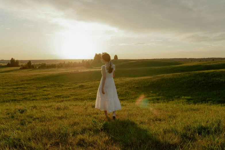 a woman standing on top of a lush green field, an album cover, inspired by Russell Drysdale, unsplash contest winner, in a long white dress, sunset light, still frame from a movie, pride and prejudice