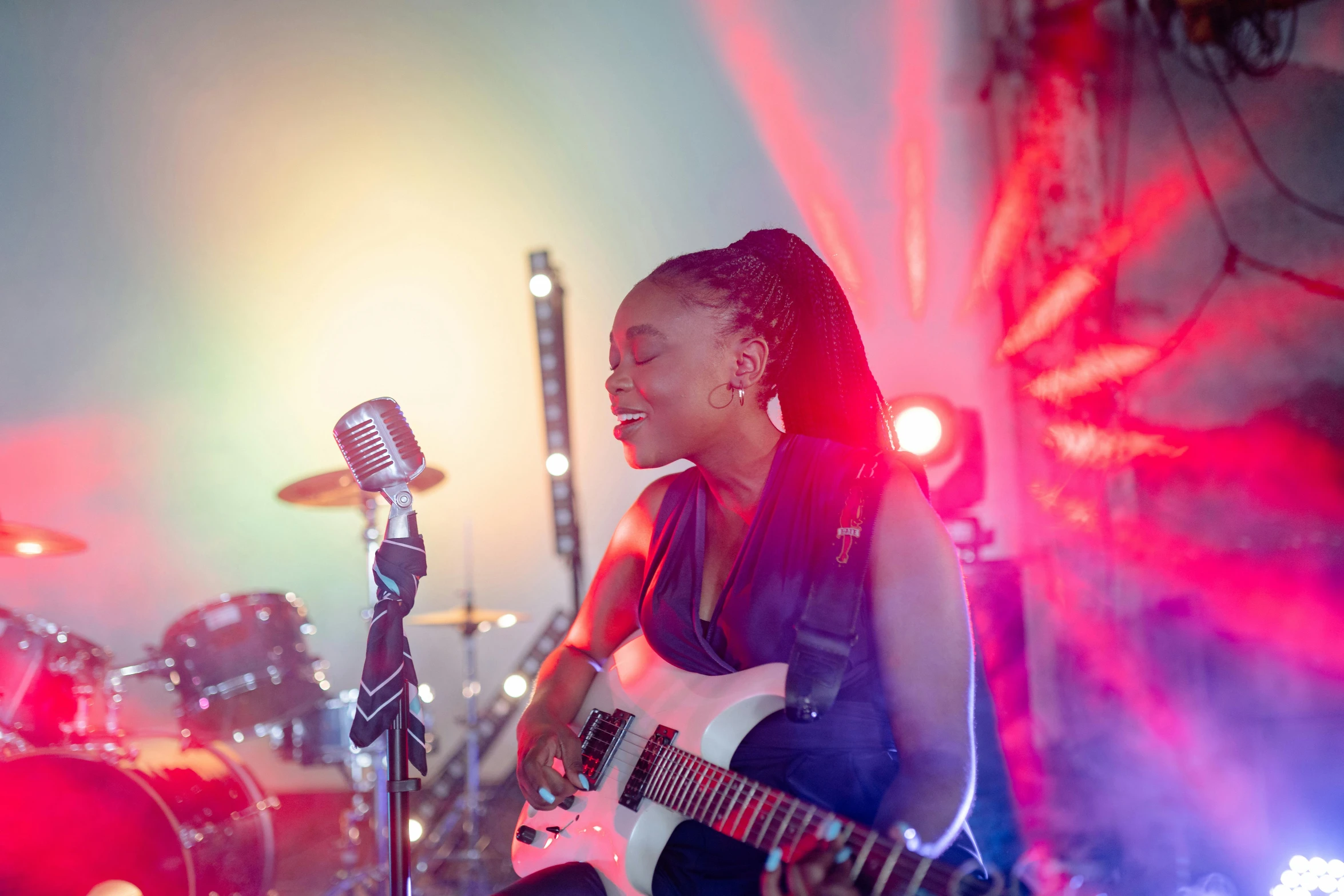 a woman playing a guitar and singing into a microphone, pexels contest winner, happening, photo of a black woman, with red haze and a massive grin, bright lights, avatar image