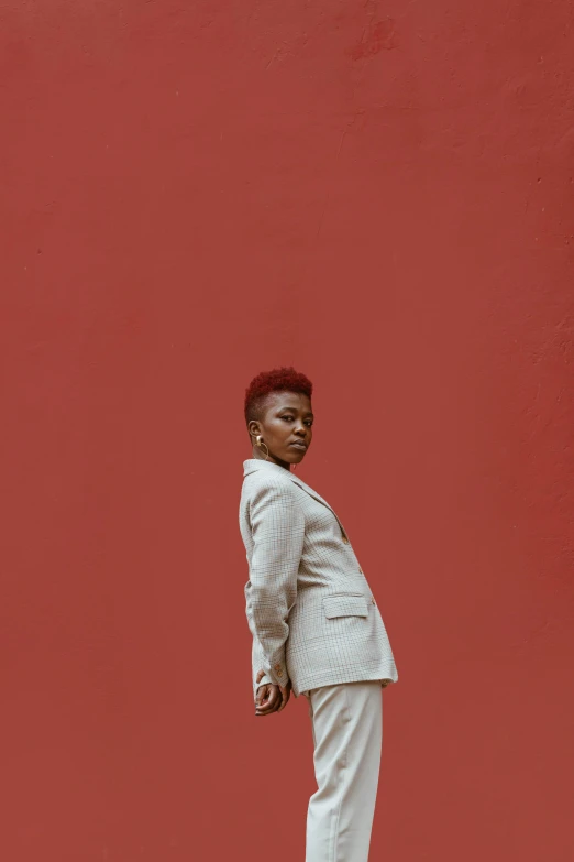 a man in a white suit standing in front of a red wall, by Cosmo Alexander, trending on pexels, african american young woman, with a mohawk, woman with red hair, 15081959 21121991 01012000 4k