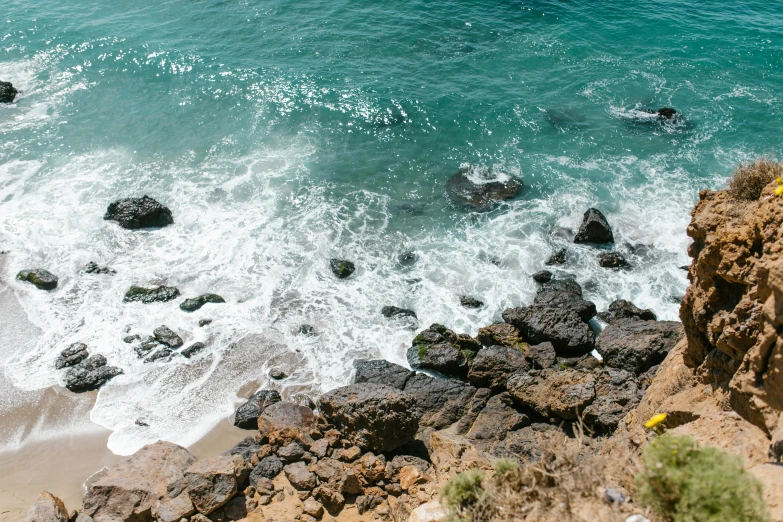 a man riding a surfboard on top of a rocky beach, pexels contest winner, malibu canyon, view from slightly above, steep cliffs, azure water