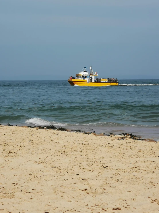 a yellow boat traveling across a body of water, on the sand, farol da barra, dredged seabed, whales showing from the waves