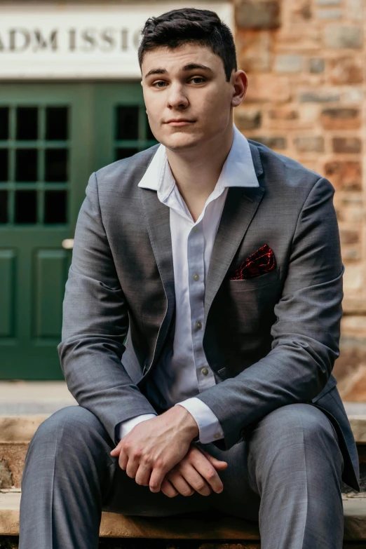 a man in a suit sitting on the steps of a building, with pale skin, lachlan bailey, payne's grey and venetian red, in gunmetal grey