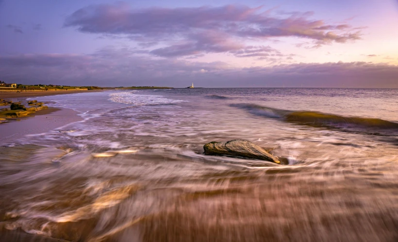 a large rock sitting on top of a sandy beach, by Julian Allen, waves and splashes, last light, bold lighthouse in horizon, conor walton