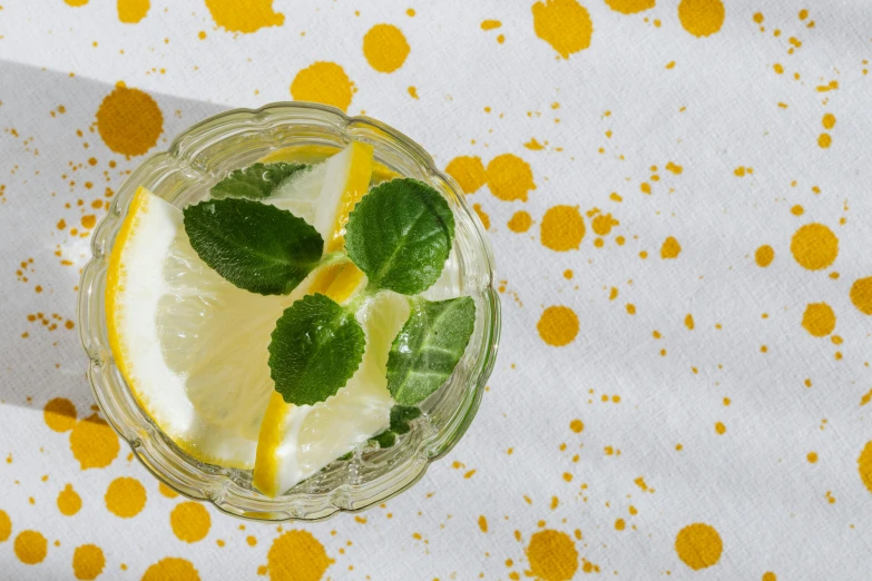 a glass of lemonade sitting on top of a table, visual art, mint leaves, white and yellow scheme, spatter, background image