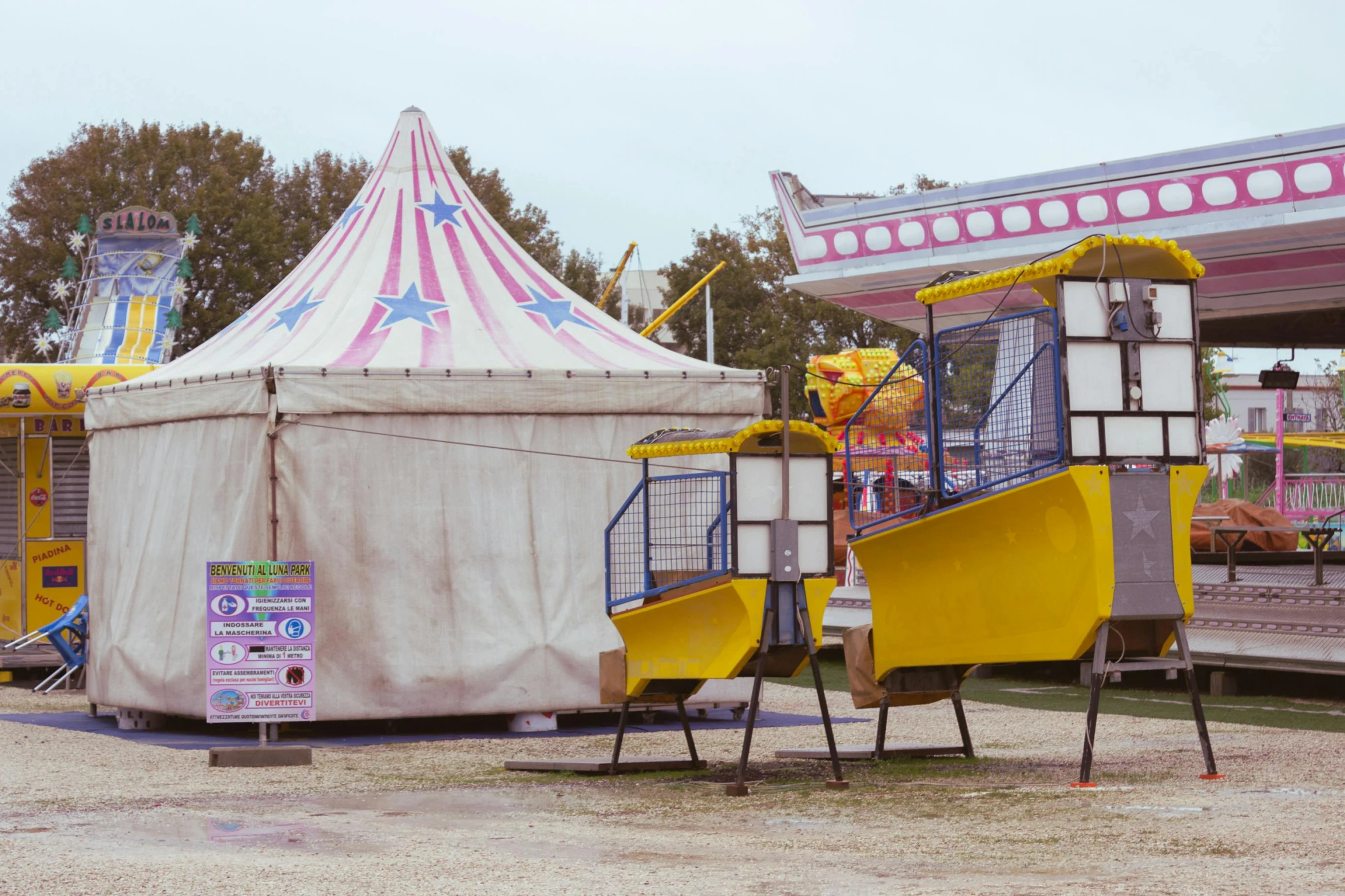 a carnival tent with a yellow slide in front of it, by The Family Circus, pexels contest winner, retro spaceships parked outside, faded and dusty, fruit machines, chairlifts