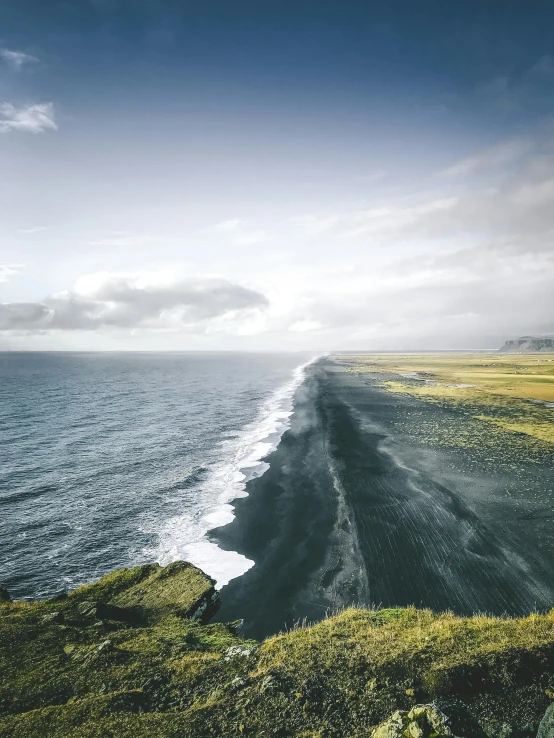a large body of water sitting on top of a lush green hillside, by Kristian Zahrtmann, pexels contest winner, black sand, overlooking the beach, nordic landscape, erosion algorithm landscape