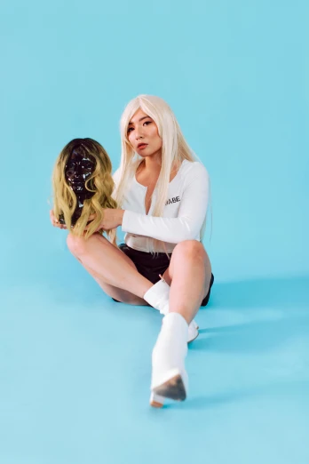 a woman with blonde hair sitting on a blue surface, an album cover, inspired by Elsa Bleda, unsplash, tifa lockhart with white hair, belle delphine, in white room, drag