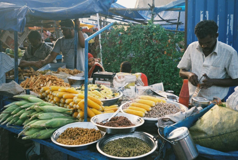 a man standing in front of a table filled with lots of food, colombo sri lankan city street, avatar image, blue and yellow fauna, 2000s photo